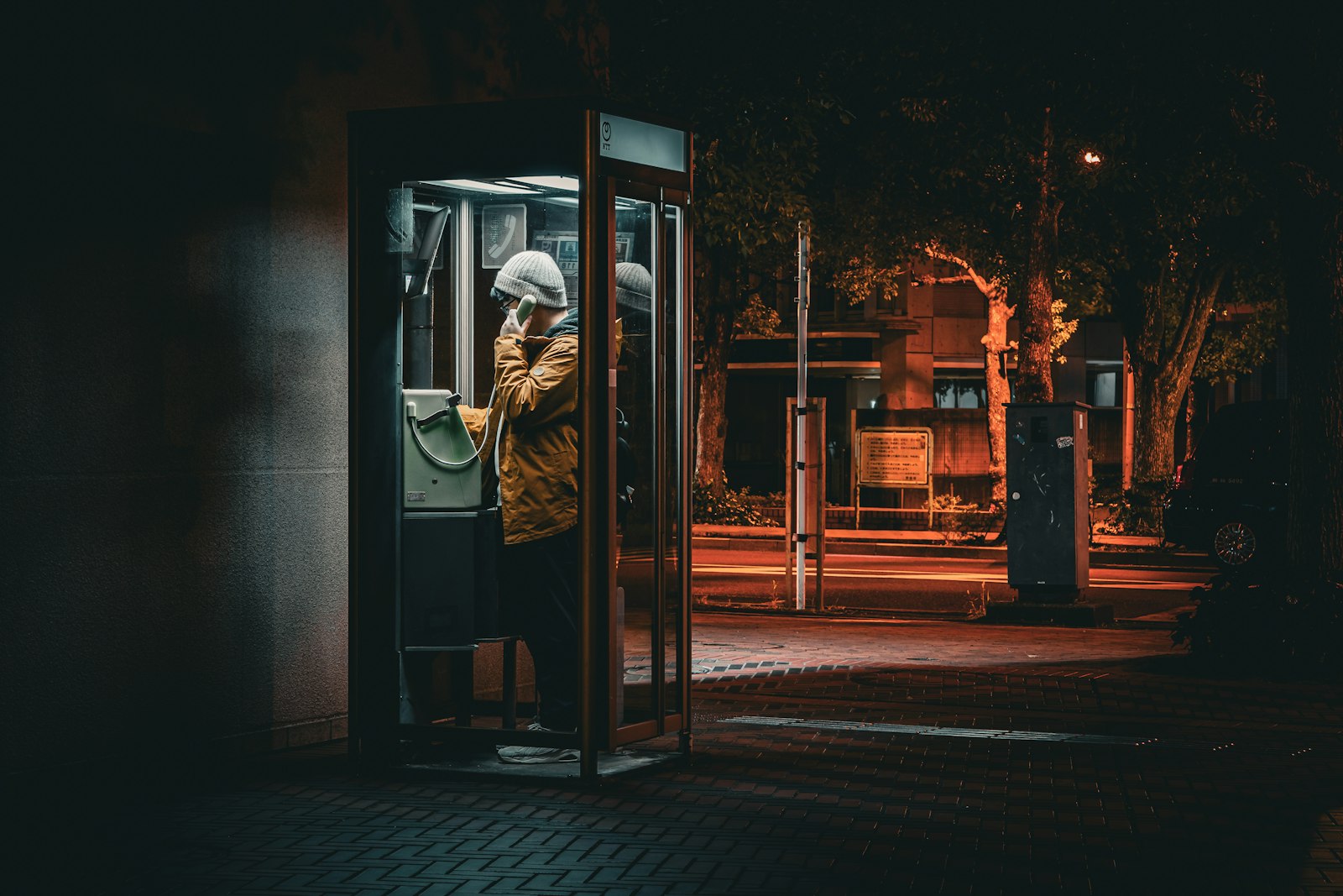A person making a call from a public phone booth at night on a Japanese street