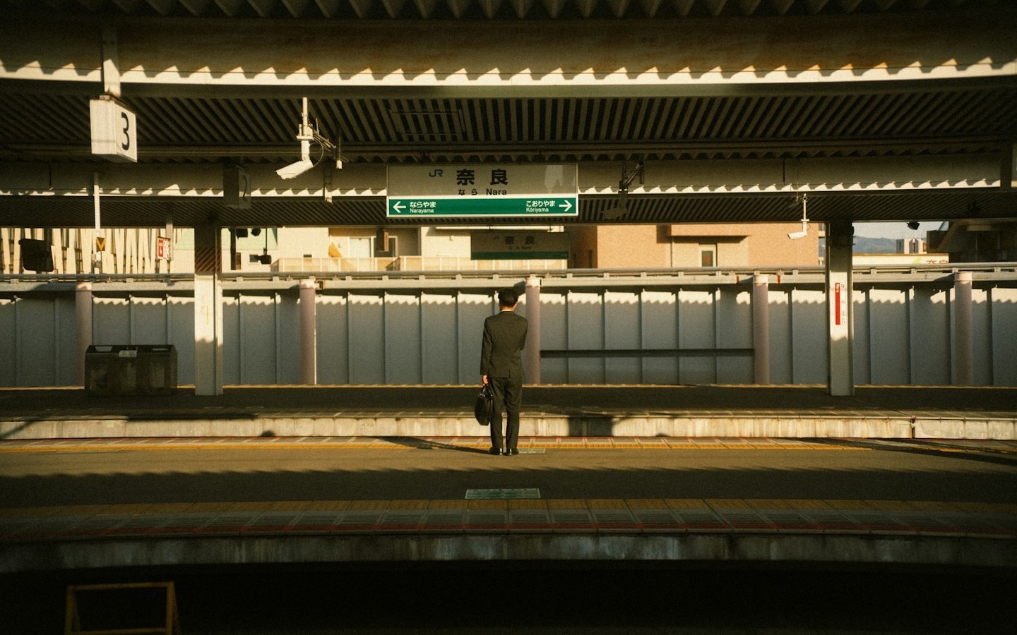 A lone traveler with a bag standing on a JR train platform in Japan at golden hour
