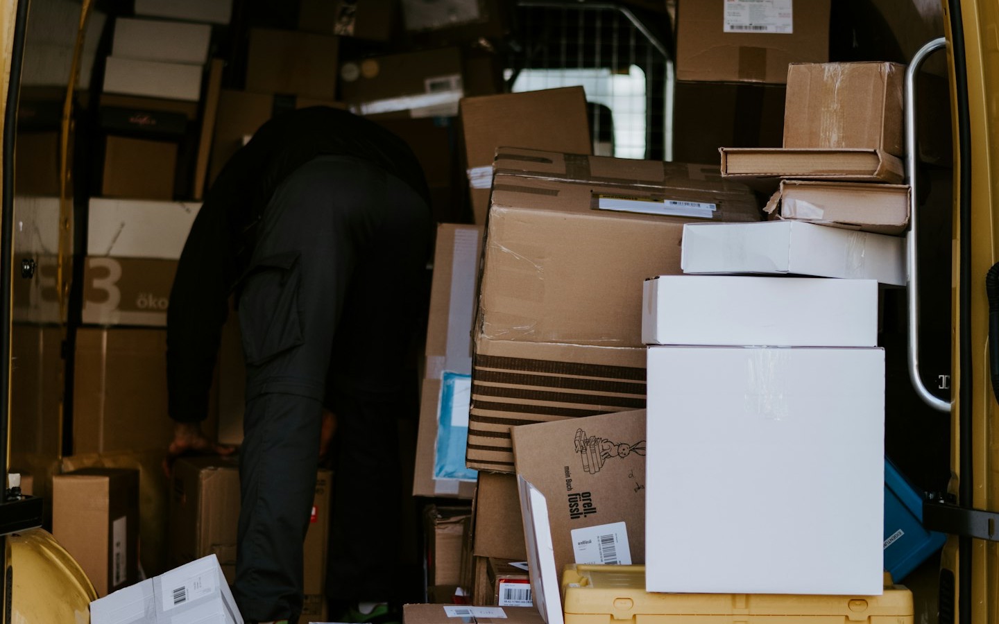The open back of a delivery van loaded with parcels, a courier sorting them