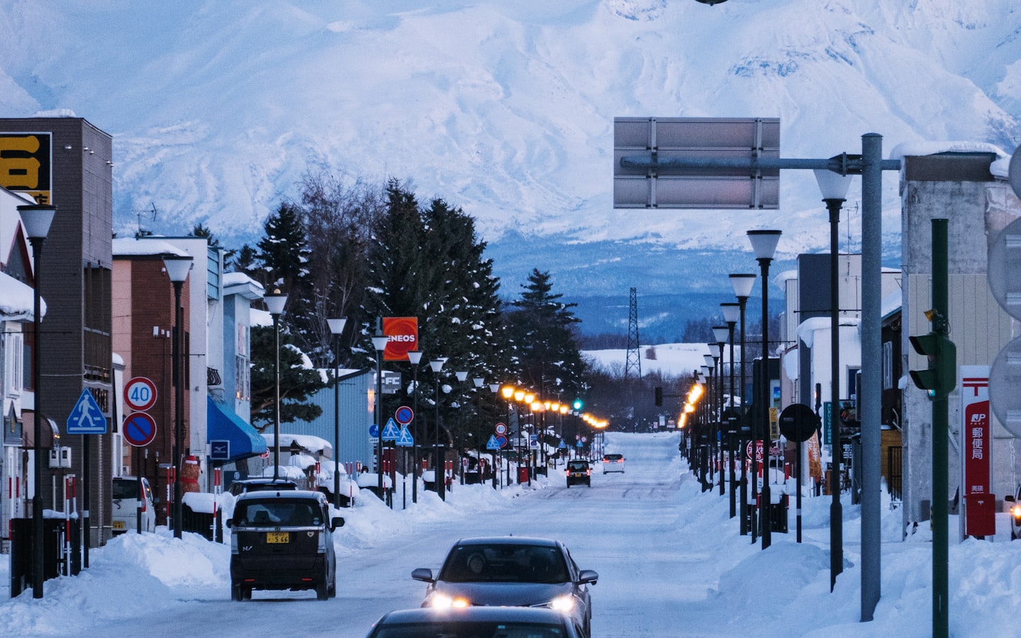 A car driving through a snowy Hokkaido town with mountains in the background