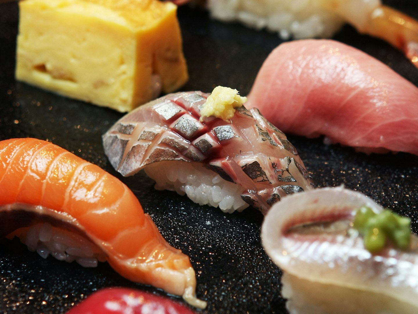 Close-up of fresh nigiri sushi — fatty tuna, salmon and horse mackerel — on a dark counter