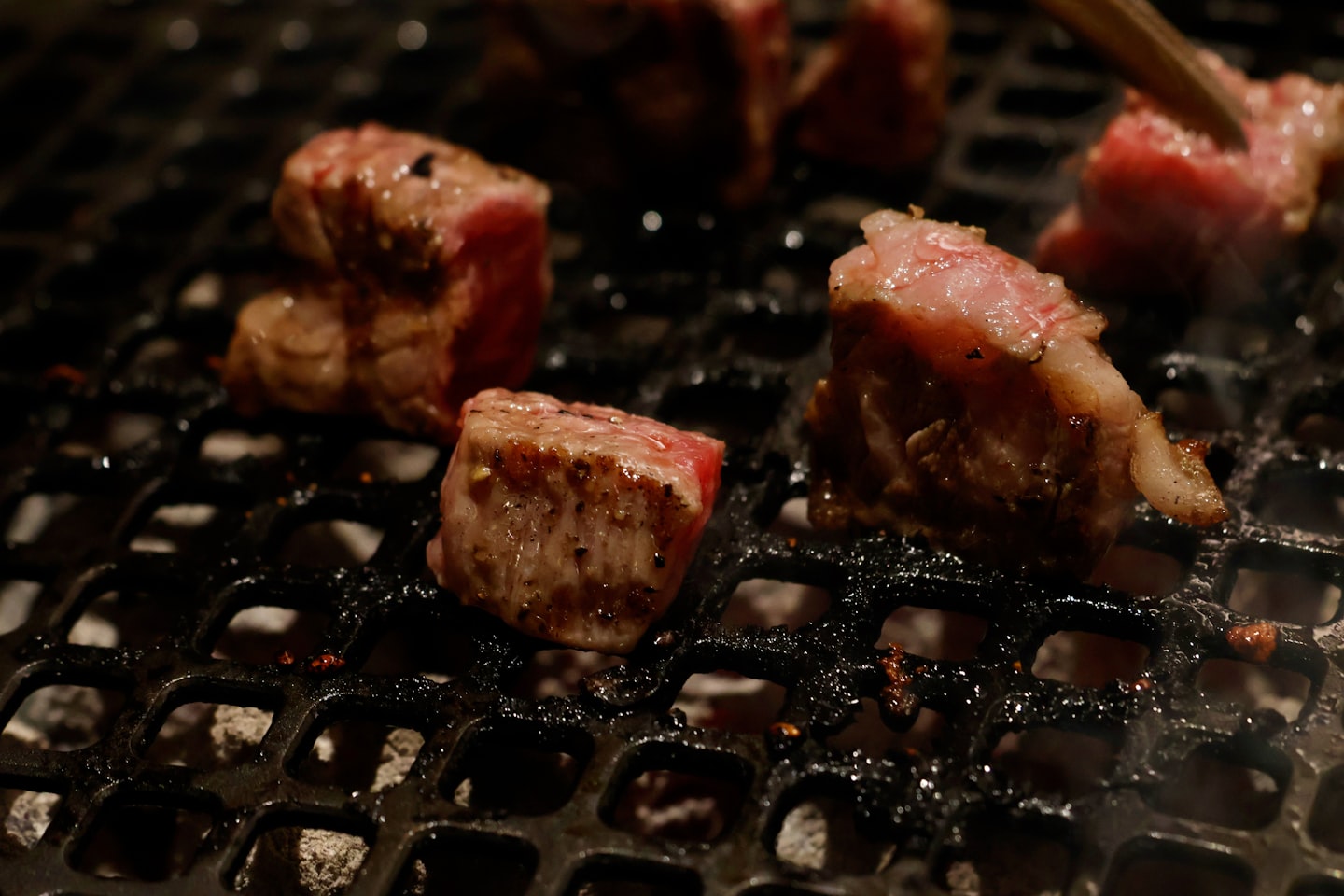 Marbled wagyu beef cubes searing on a charcoal yakiniku grill