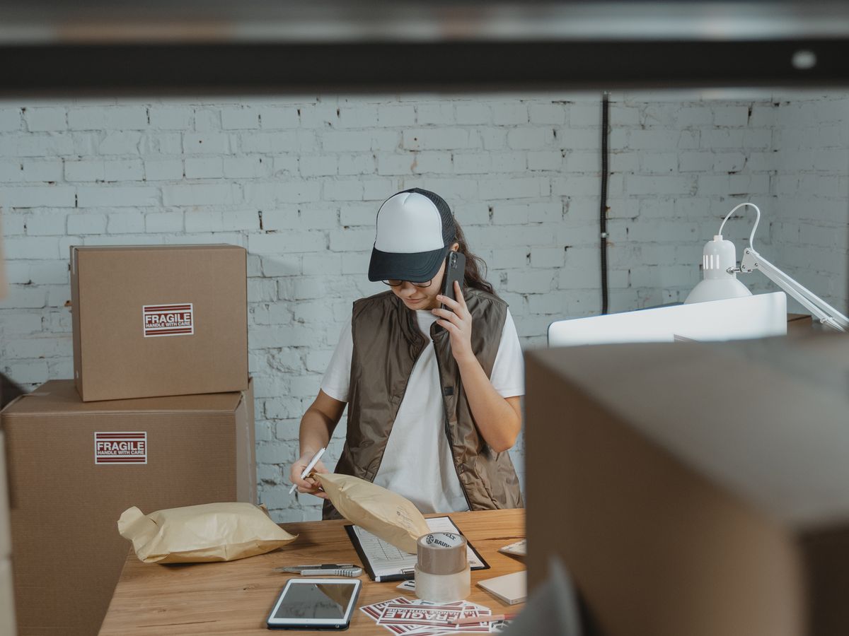 A seller on a phone call at a desk surrounded by parcels, tape and shipping labels