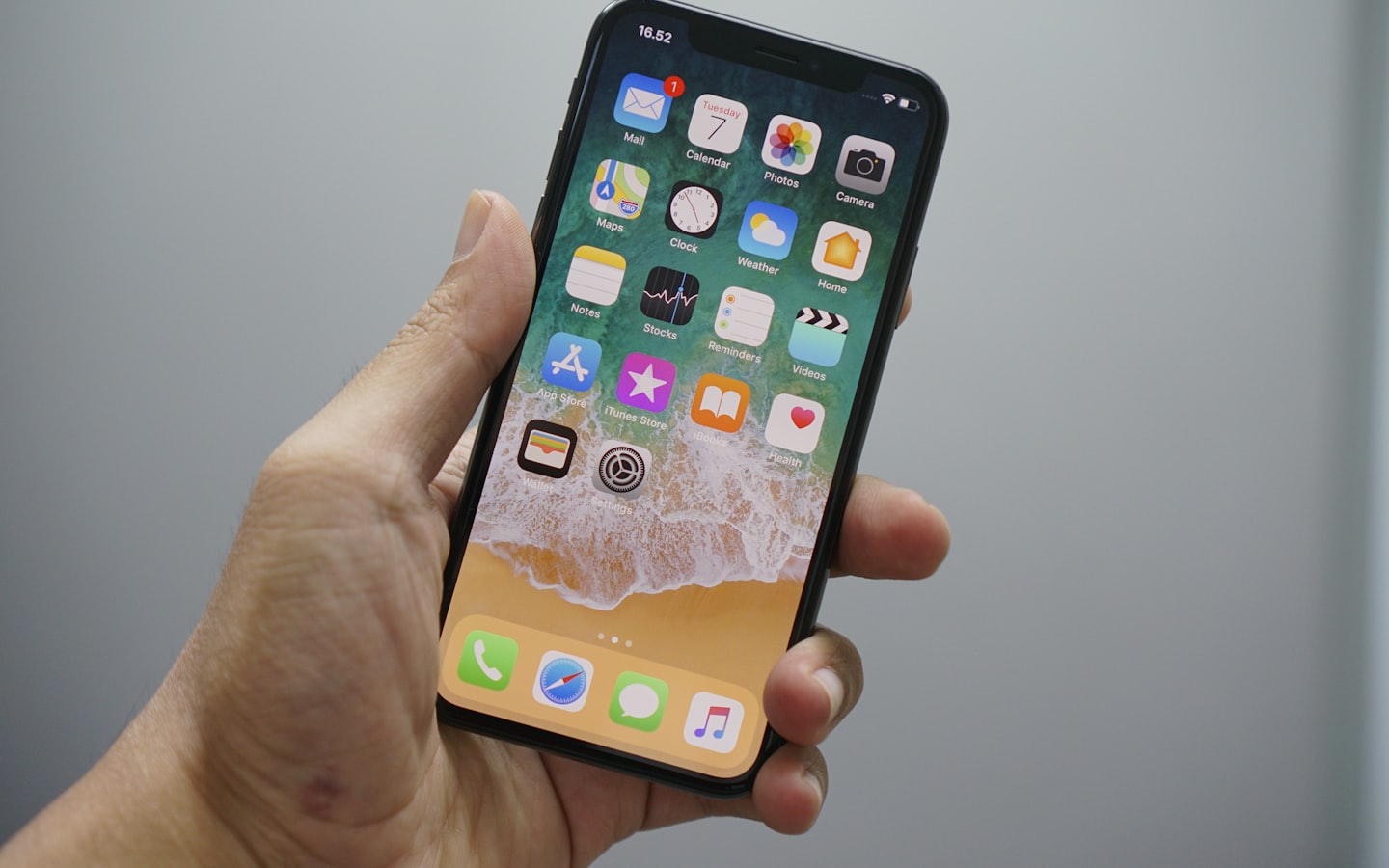 A hand holding an iPhone showing the iOS home screen